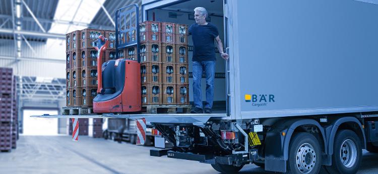 Kierowca samochodu ciężarowego rozładowuje napoje i elektryczny wózek paletowy za pomocą windy załadowczej BAR w hali
