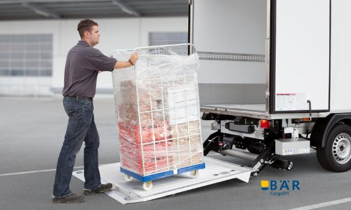 Mężczyzna wsuwa kontenery rolkowe na platformę windy załadowczej BAR zamontowanej na samochodzie dostawczym.