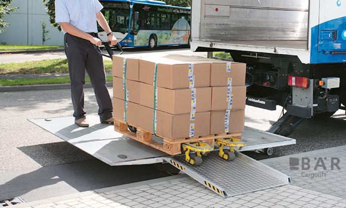 Kierowca wjeżdża na platformę windy załadowczej Bar przez mostek przeładunkowy na chodniku.